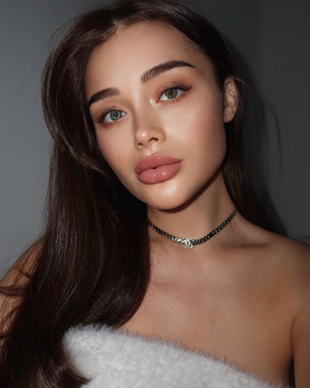 Sasha faces the camera in a white strapless fuzzy top and beaded choker, with long dark hair against a plain gray background.